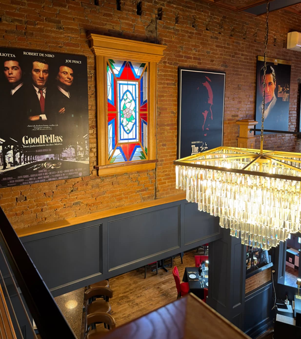Two-story dining room with exposed brick, stained glass window, crystal chandelier, and classic movie posters
