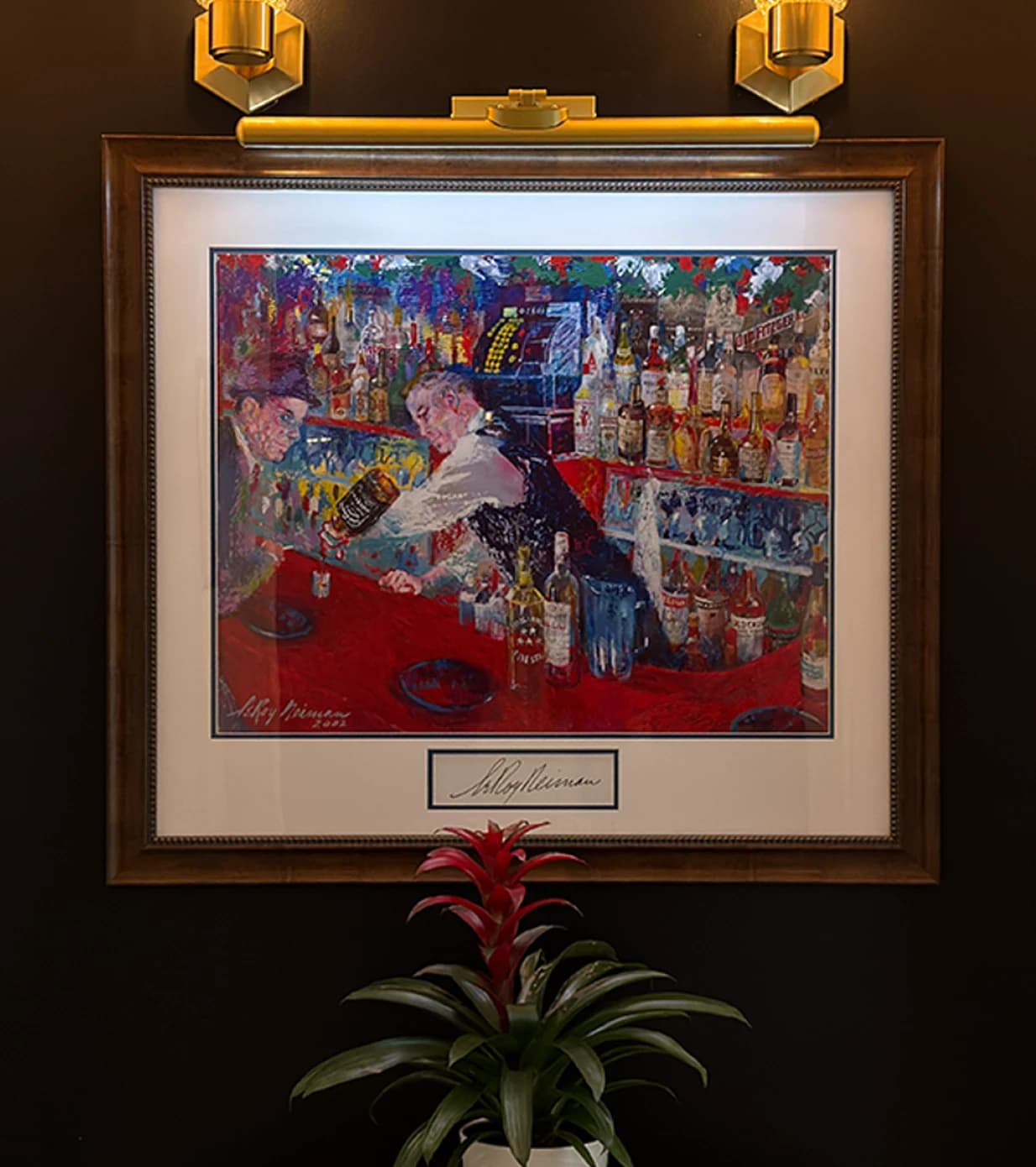 Framed LeRoy Neiman bartender painting displayed on a dark wall with brass picture lights